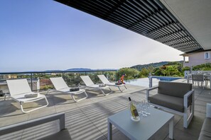 A rooftop terrace with white lounge chairs, a table with a bottle and glasses, and a pool in the background. - Villa sea view Saint-Cyprien (Zonza)