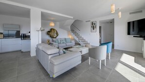 Ein modernes Wohnzimmer mit Sofa, Couchtisch und Sesseln. Eine Treppe führt zu einer weiteren Ebene.