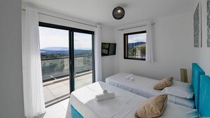 Ein Hotelzimmer mit zwei Betten, einem Balkon mit Stadtblick, einem Flachbildfernseher und einer Deckenleuchte.