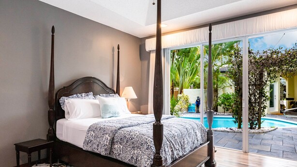 Une chambre à coucher avec un lit à baldaquin, une table de chevet et une vue sur une piscine, visible à travers de grandes portes vitrées.