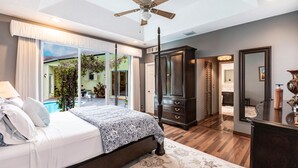 Une chambre dotée d’un grand lit, d’un ventilateur de plafond, d ’une armoire en bois foncé et donnant sur une piscine.