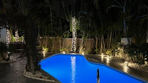 Une piscine à bord incurvé, entourée d’une terrasse en pierre et de plantes tropicales.