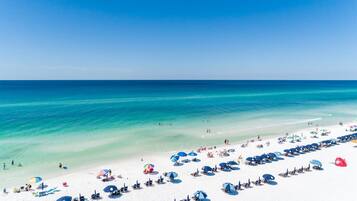 A beach with white sand, clear turquoise water, and numerous umbrellas.