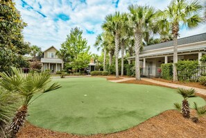 Un campo de golf con un césped bien cuidado, rodeado de palmeras y un edificio residencial.