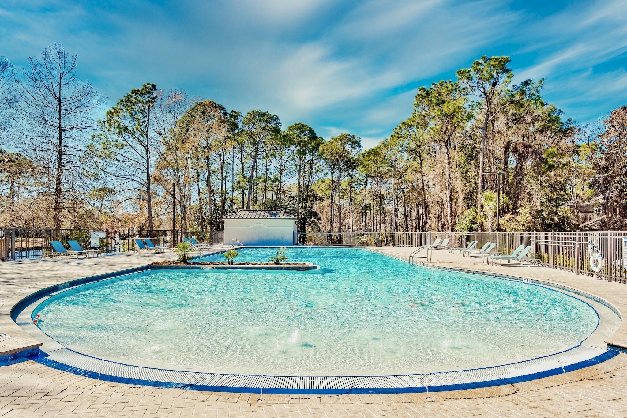 Une piscine aux eaux cristallines, entourée d’arbres, avec des chaises longues et une bouée de sauvetage disposée le long du bord.