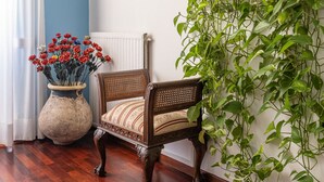 A room with a wooden floor, a chair with a striped cushion, a large vase with red flowers, and a painting of cliffs on the wall. - LA VITA E' BELLA (Sorrento)
