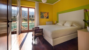 A bedroom with a bed, a chair, a nightstand, a painting, and a view of a balcony with plants and a railing. - LA VITA E' BELLA (Sorrento)