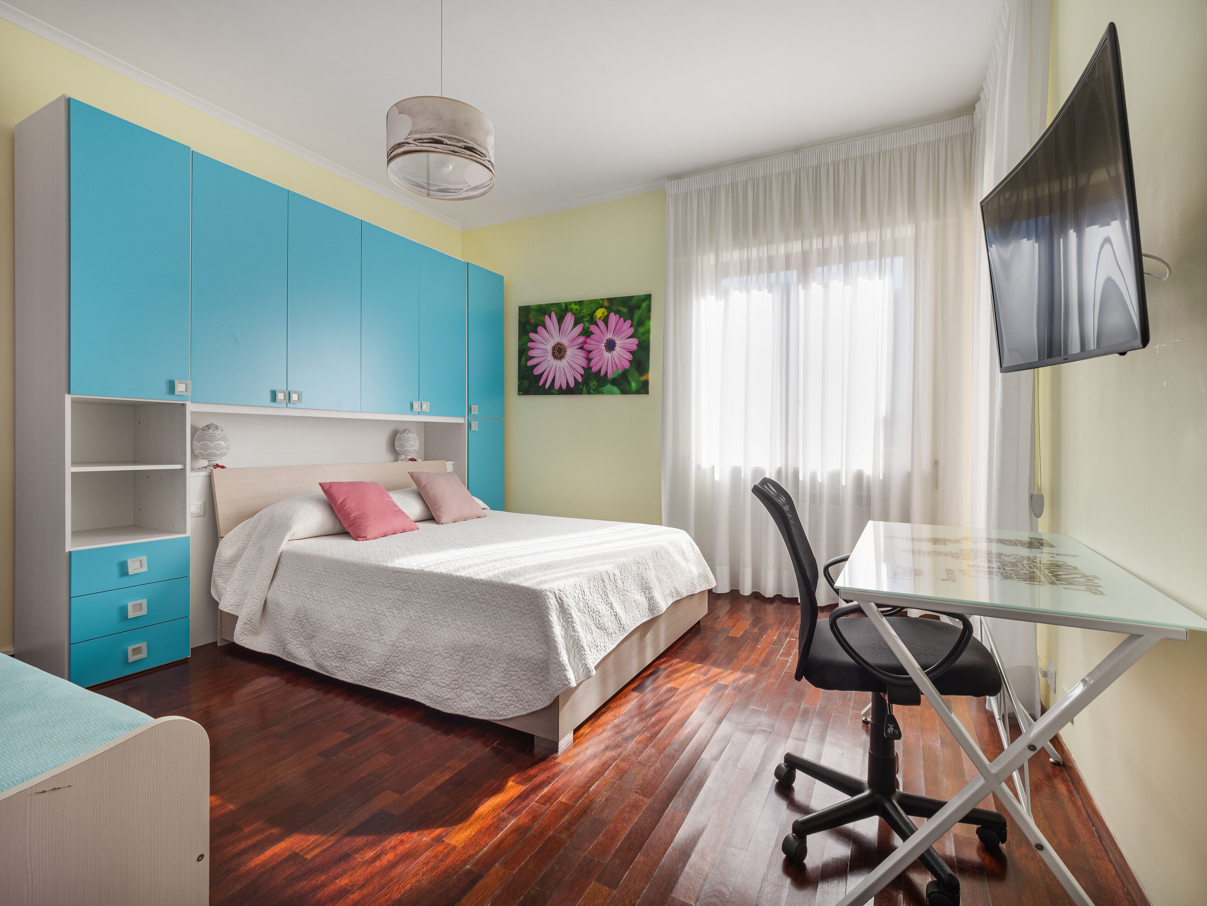 Un dormitorio con cama, un escritorio con silla, televisor y ventana con cortinas.