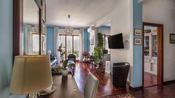 A spacious living room with a wooden floor, a large mirror, a sofa, a coffee table, and a TV mounted on the wall. - LA VITA E' BELLA (Sorrento)
