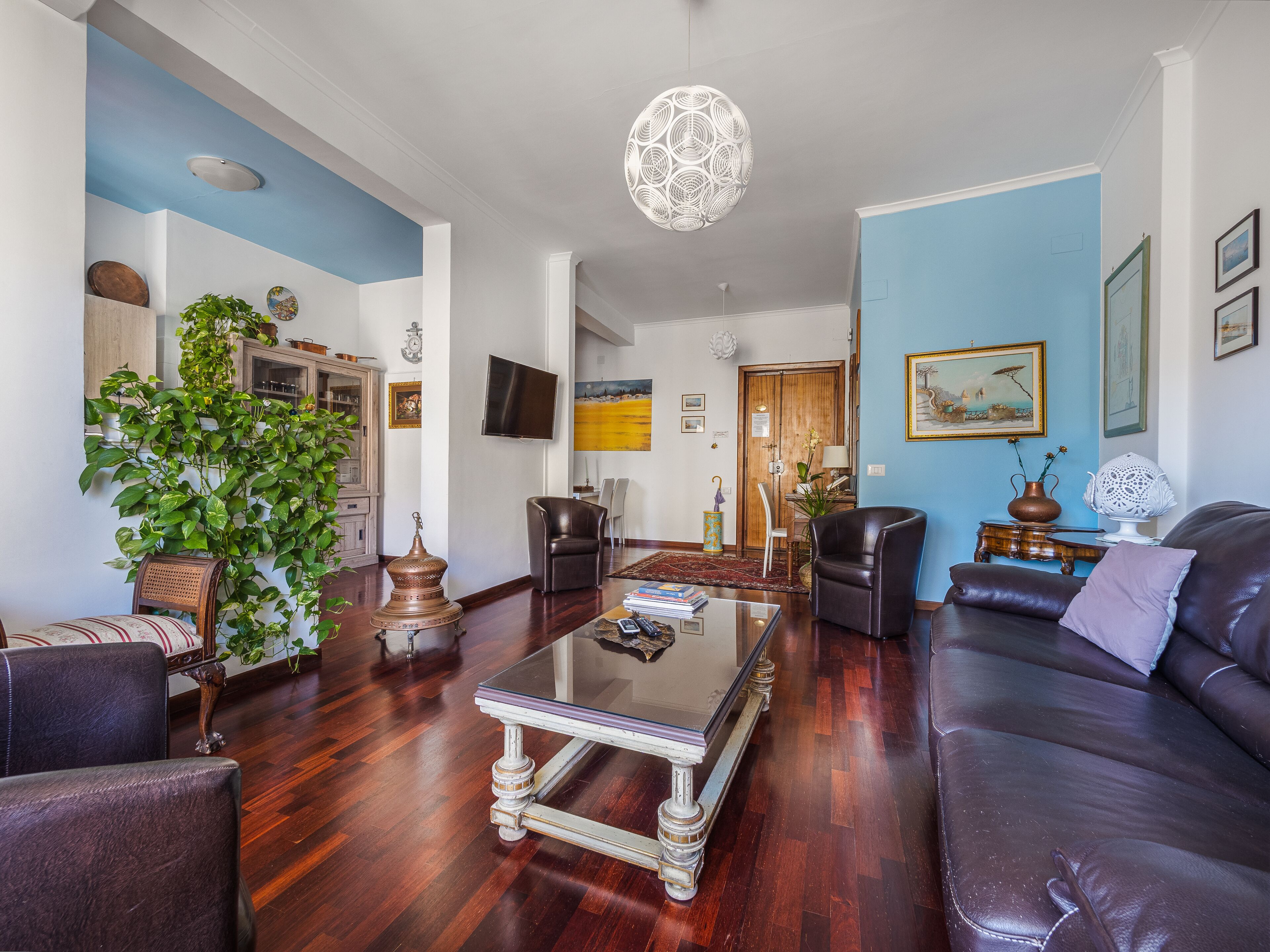 A living room with a glass coffee table, leather sofas, a wooden cabinet, and a large plant.