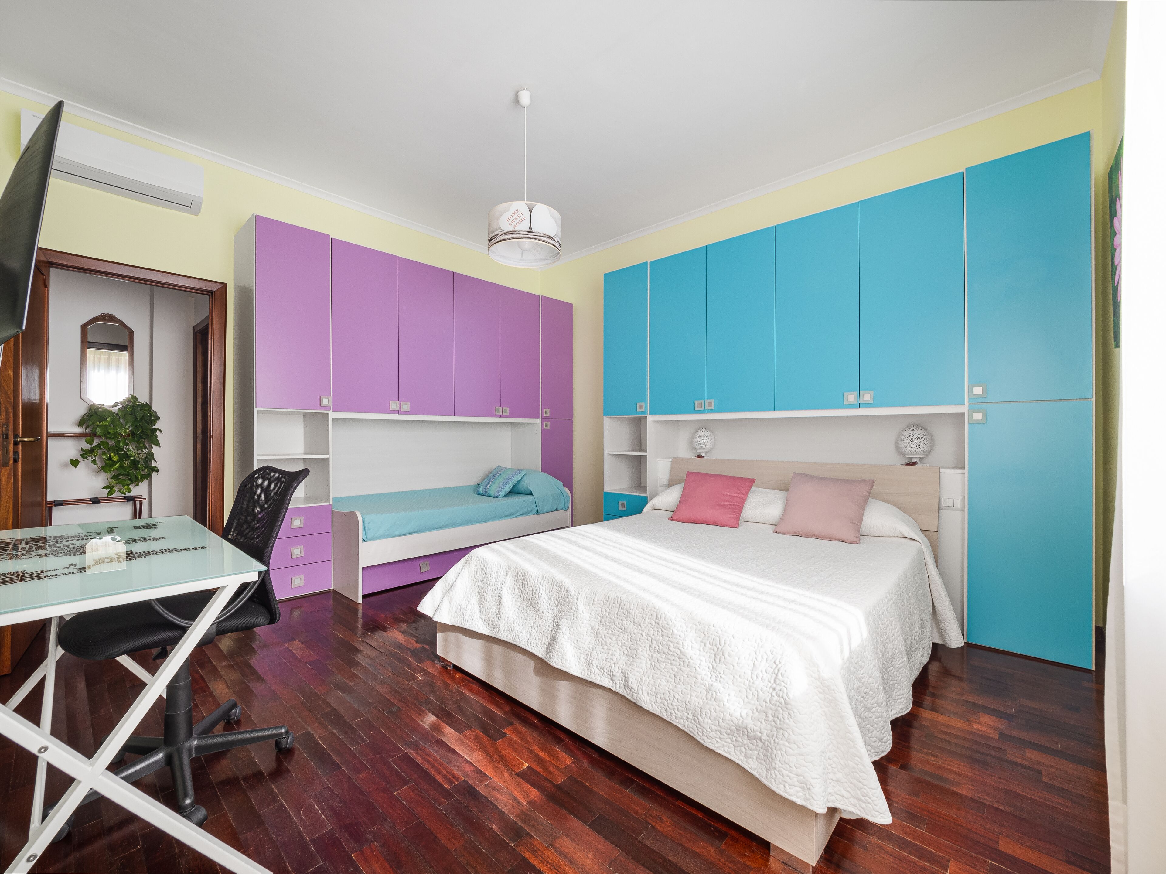 A bedroom with a bed, two desks, a chair, and a wardrobe.