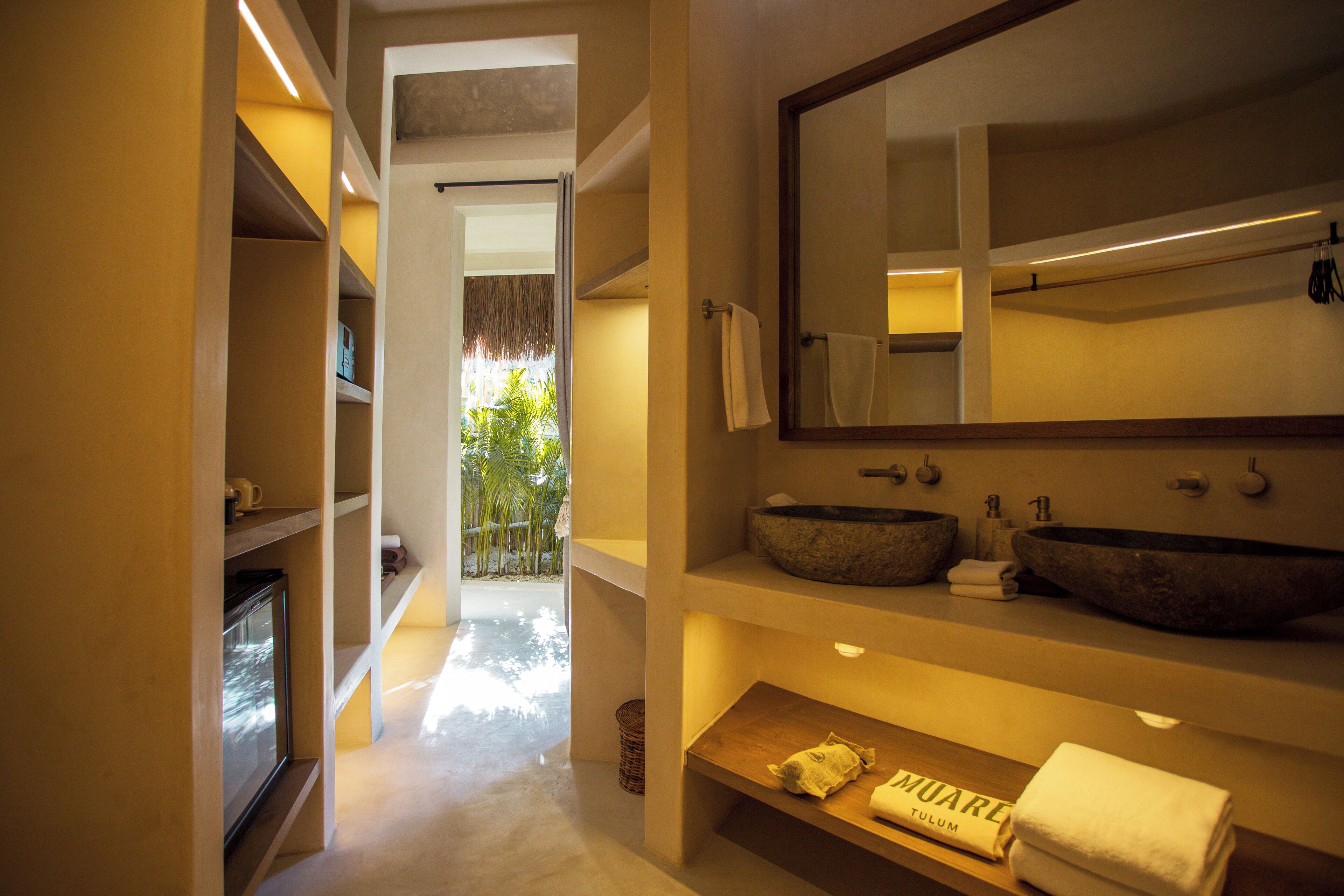 Un baño moderno con un espejo grande, dos lavamanos de piedra y un estante de madera con toallas.