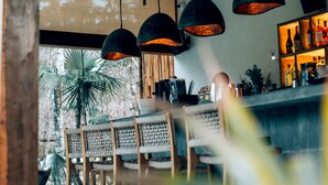 Een restaurant met een rustiek plafond, hangende吊り下げ式lampen, rieten stoelen en een bar met flessen.