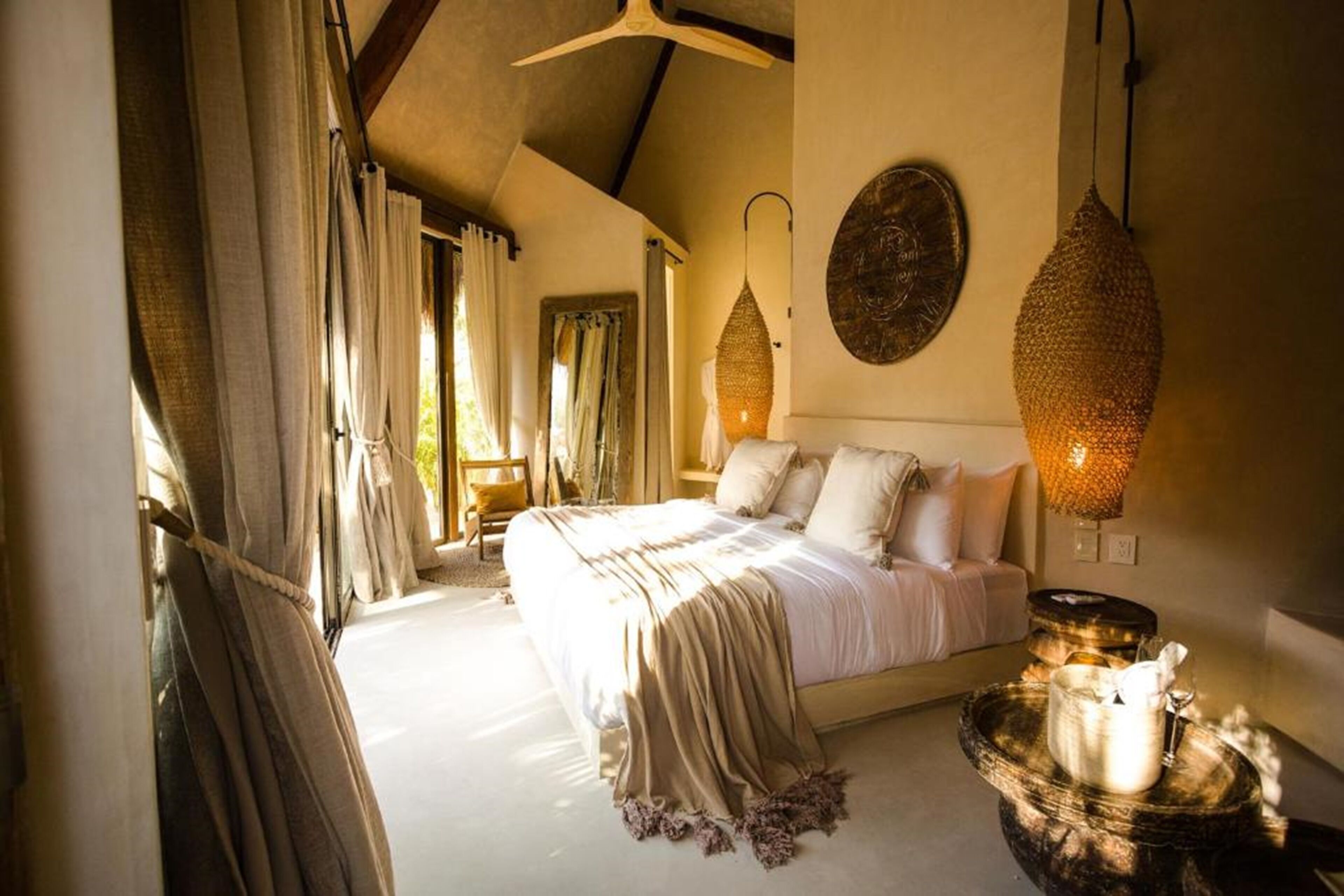 A bedroom with a large bed, curtains, a hanging light fixture, and a decorative wall piece.