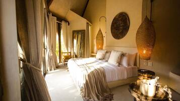A bedroom with a large bed, curtains, a hanging light fixture, and a decorative wall piece.