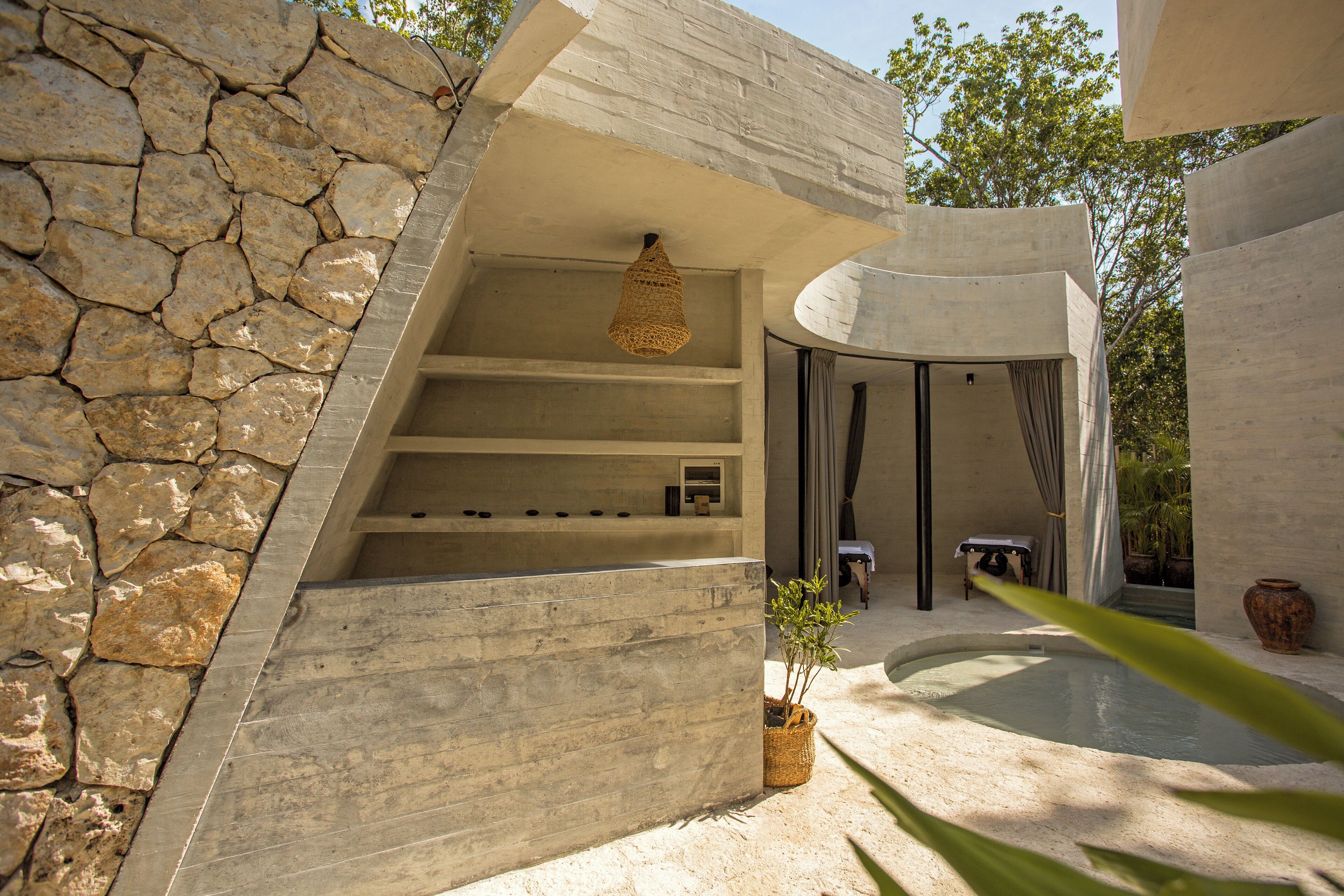 A modern building with a stone wall, a hanging light fixture, a pool, and a potted plant.