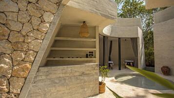 A modern building with a stone wall, a hanging light fixture, a pool, and a potted plant.