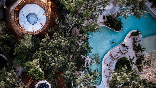 Vista aérea de un complejo turístico con varias estructuras circulares, una piscina central y zonas de descanso alrededor.
