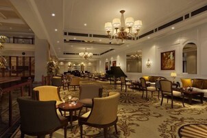 Un espacioso vestíbulo de hotel con varias zonas de estar, candelabros y un piano de cola.