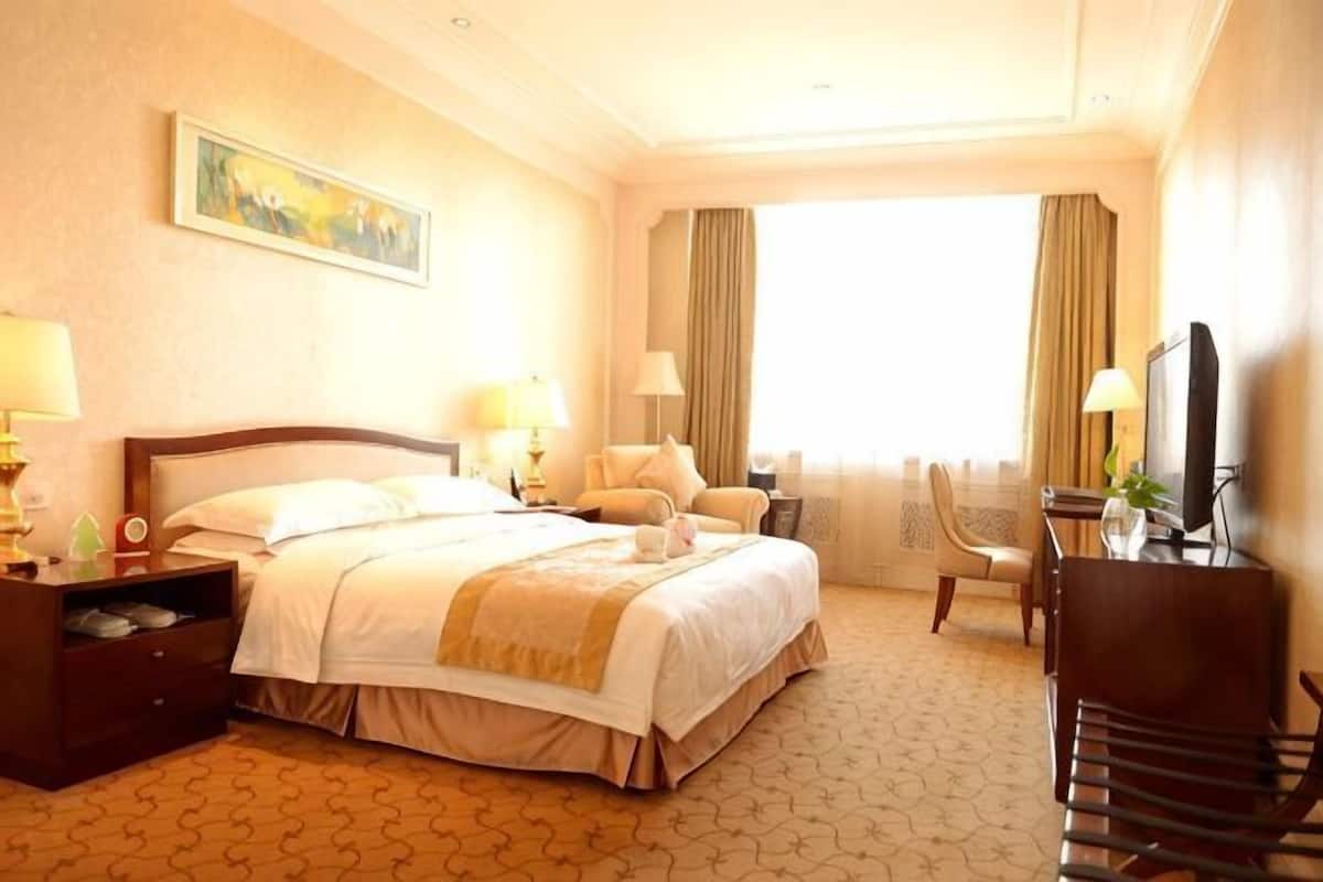 Ein Hotelzimmer mit einem Bett, Nachttischen, einem Schreibtisch, einem Sessel, einem Fernseher und einem Fenster mit Vorhängen.