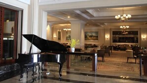 A grand lobby with a black grand piano, marble flooring, and elegant chandeliers.