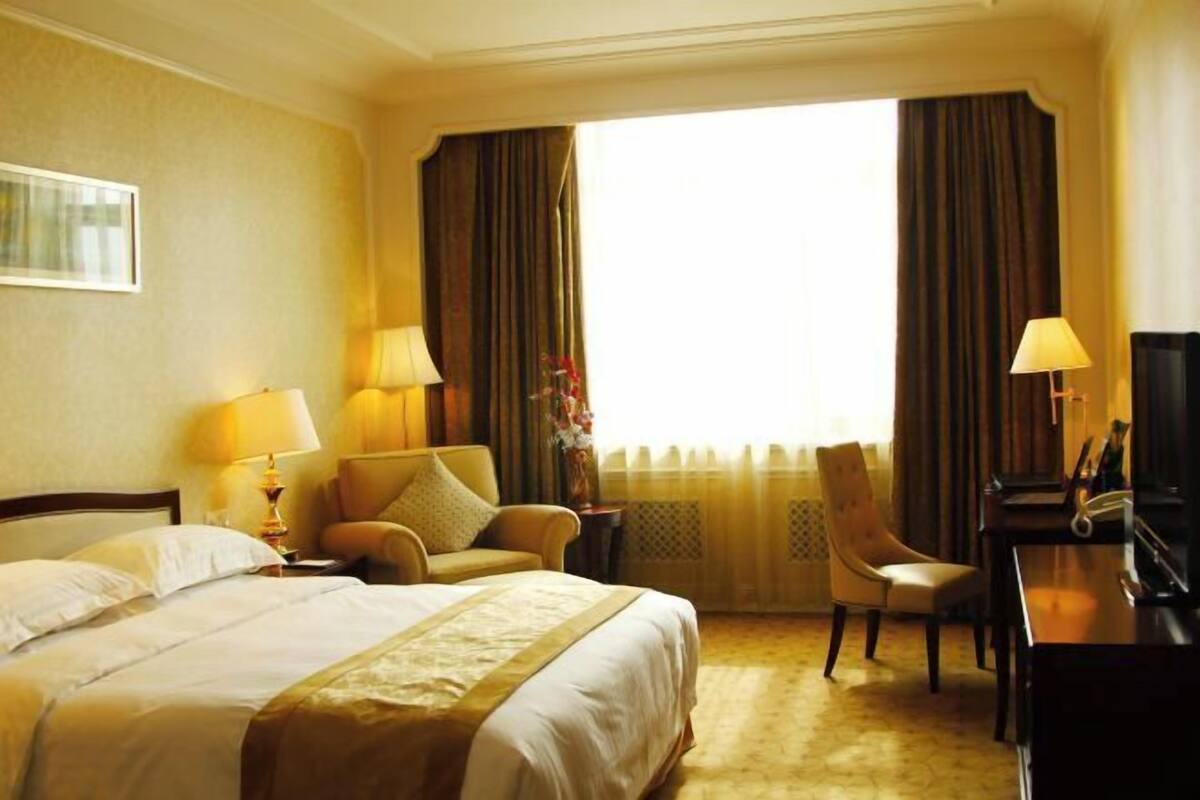 Ein Hotelzimmer mit einem Bett, zwei Stühlen, einem Schreibtisch und einem großen Fenster mit Vorhängen.