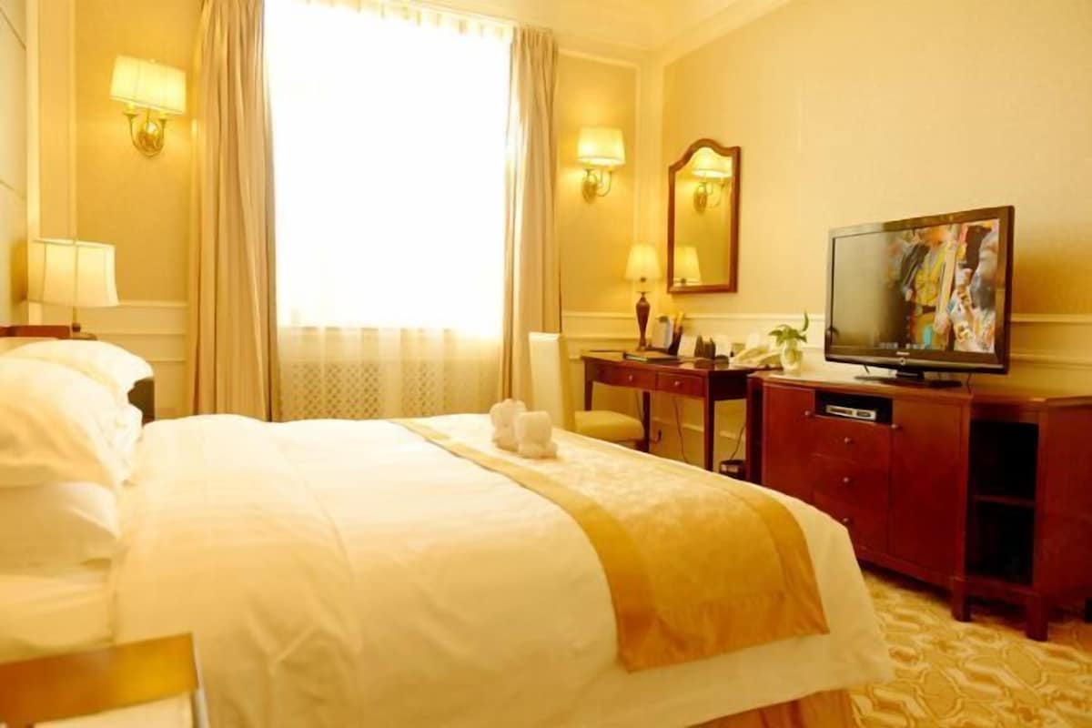 Une chambre d’hôtel avec un grand lit, un bureau avec une télévision et une fenêtre avec des rideaux.