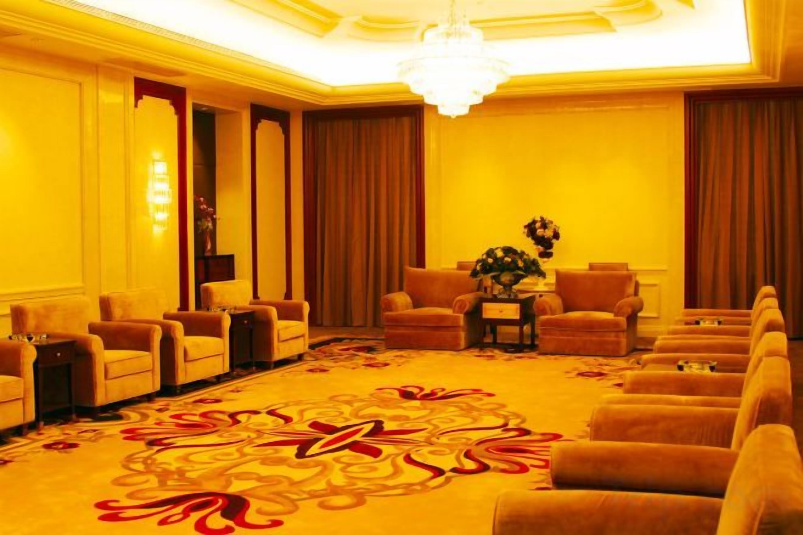 Una habitación de hotel con una alfombra grande y estampada, varios sillones, un sofá y una araña.
