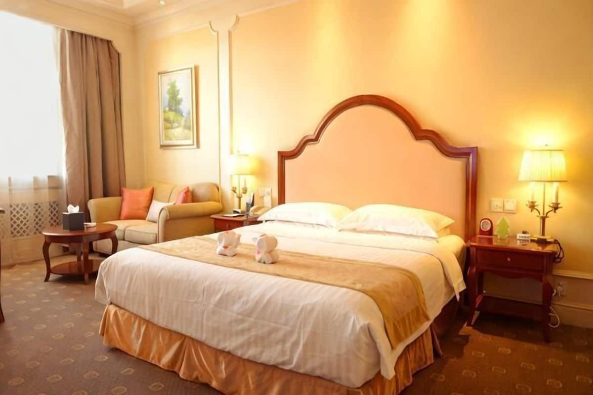 Ein Hotelzimmer mit einem großen Bett, Nachttischen, einem Sessel, einer Lampe und einem Gemälde an der Wand.