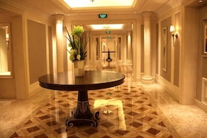 Corredor de hotel com uma mesa redonda, colunas e piso estampado.