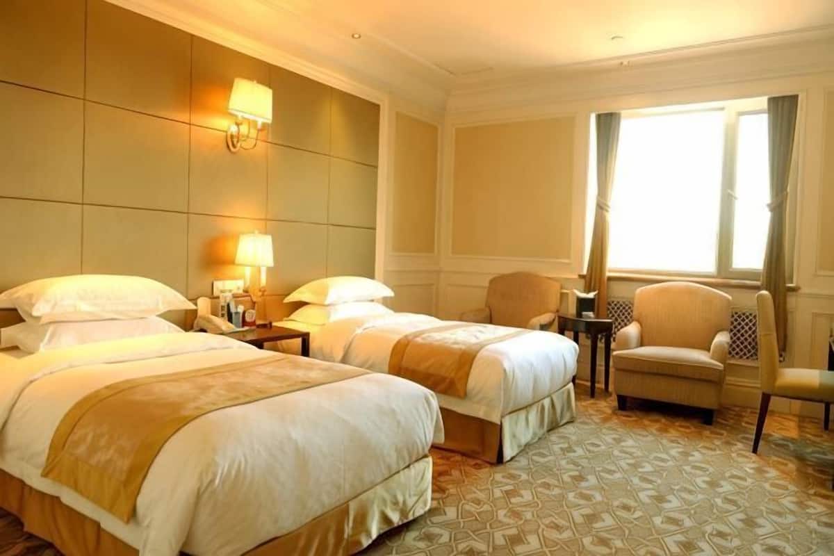 Ein Hotelzimmer mit zwei Betten, einer Sitzecke mit einem Sessel, einem kleinen Tisch und einem Fenster mit Vorhängen.