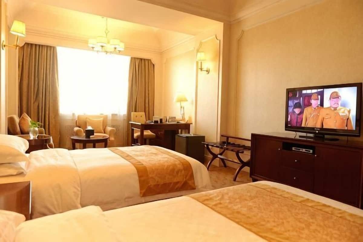 Ein Hotelzimmer mit zwei Betten, einem Schreibtisch, einem Fernseher und einem Fenster mit Vorhängen.