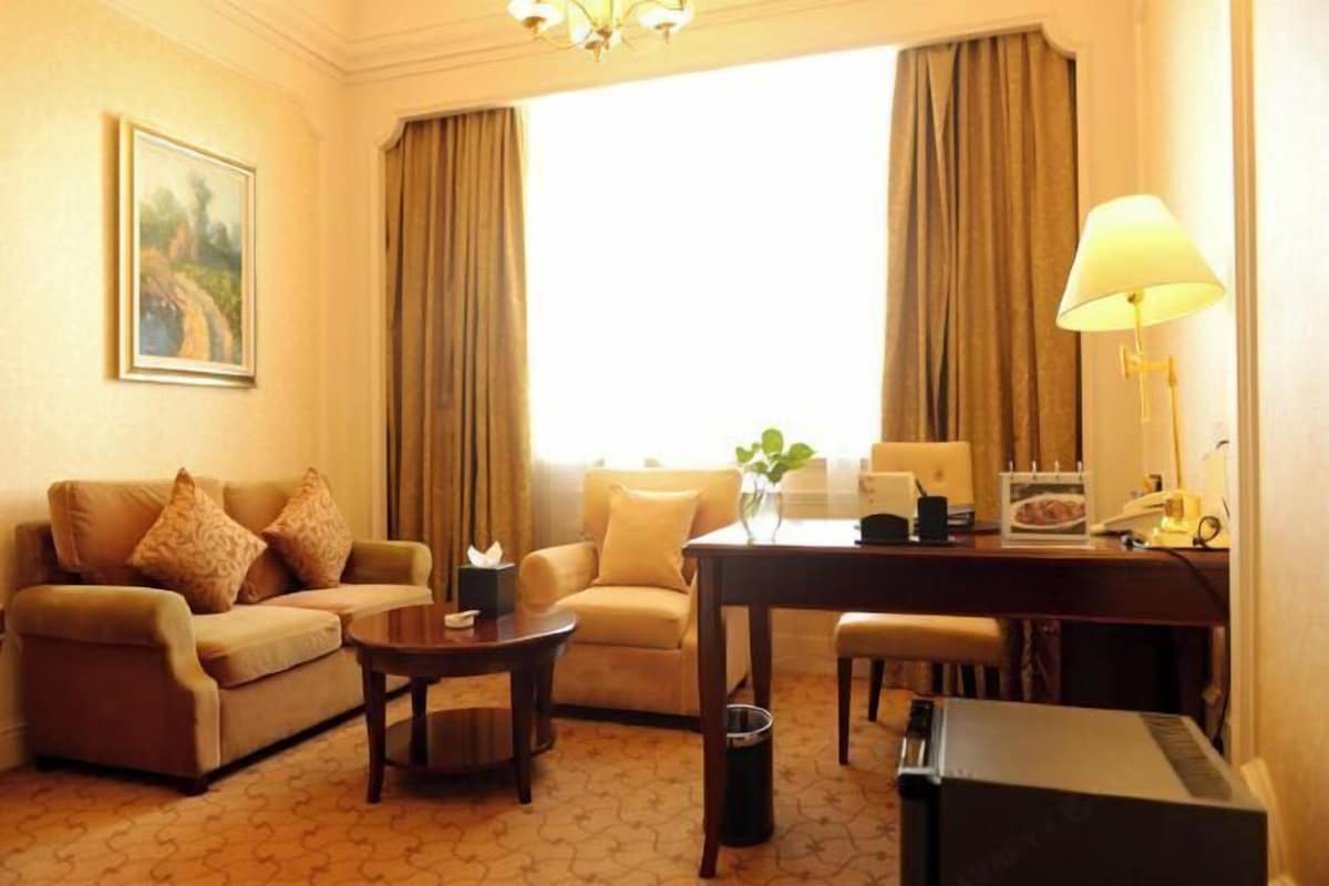 Une chambre d’hôtel avec un canapé, un fauteuil, une petite table, un bureau, une lampe et un tableau au mur.