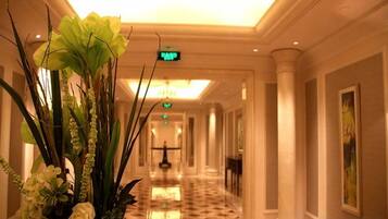 Un pasillo de hotel con piso de mármol pulido, un letrero de salida verde y un gran arreglo floral.
