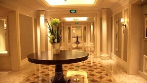 A hotel corridor with a round table, columns, and a patterned floor.