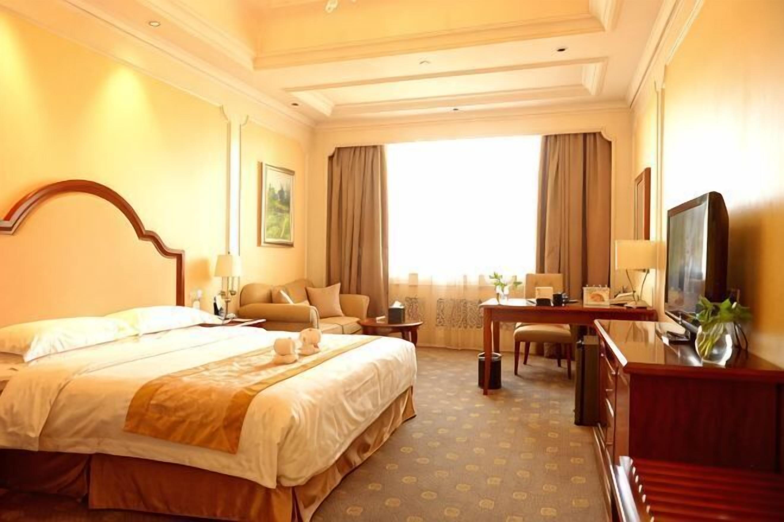 Ein Hotelzimmer mit einem großen Bett, einem Schreibtisch mit Stuhl, einem Fernseher und einem Fenster mit Vorhängen.