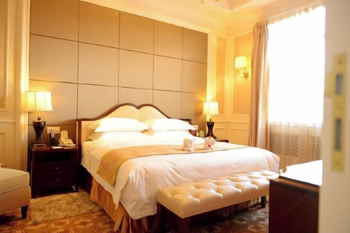 Ein Hotelzimmer mit einem großen Bett, Nachttischlampen, einem kleinen Tisch und einem Fenster mit Vorhängen.