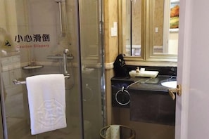 Une salle de bain avec une douche à parois de verre, une serviette suspendue à un porte-serviettes, un lavabo avec un plan de travail noir et un miroir au-dessus du lavabo.