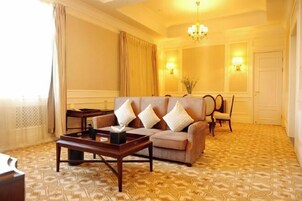 Una habitación de hotel con alfombra estampada, un sofá con cojines, una mesa de centro, una silla y una araña.