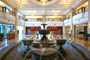 Une fontaine à plusieurs niveaux se trouve dans un vaste hall d’entrée agrémenté de lustres, doté d’un plafond haut et présentant un design architectural moderne.
