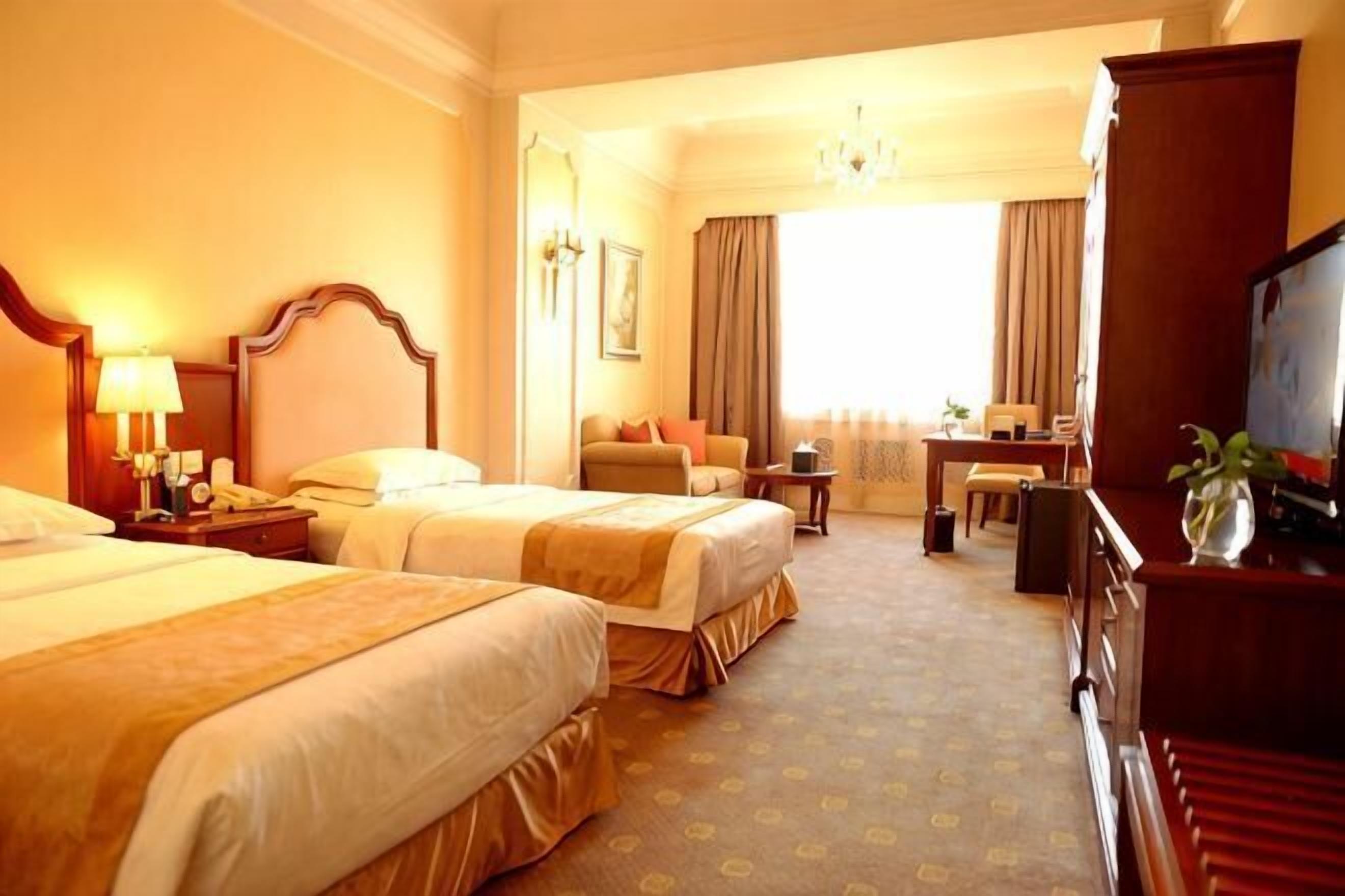 Une chambre d’hôtel avec deux lits, un bureau, une chaise, une télévision et une grande fenêtre.