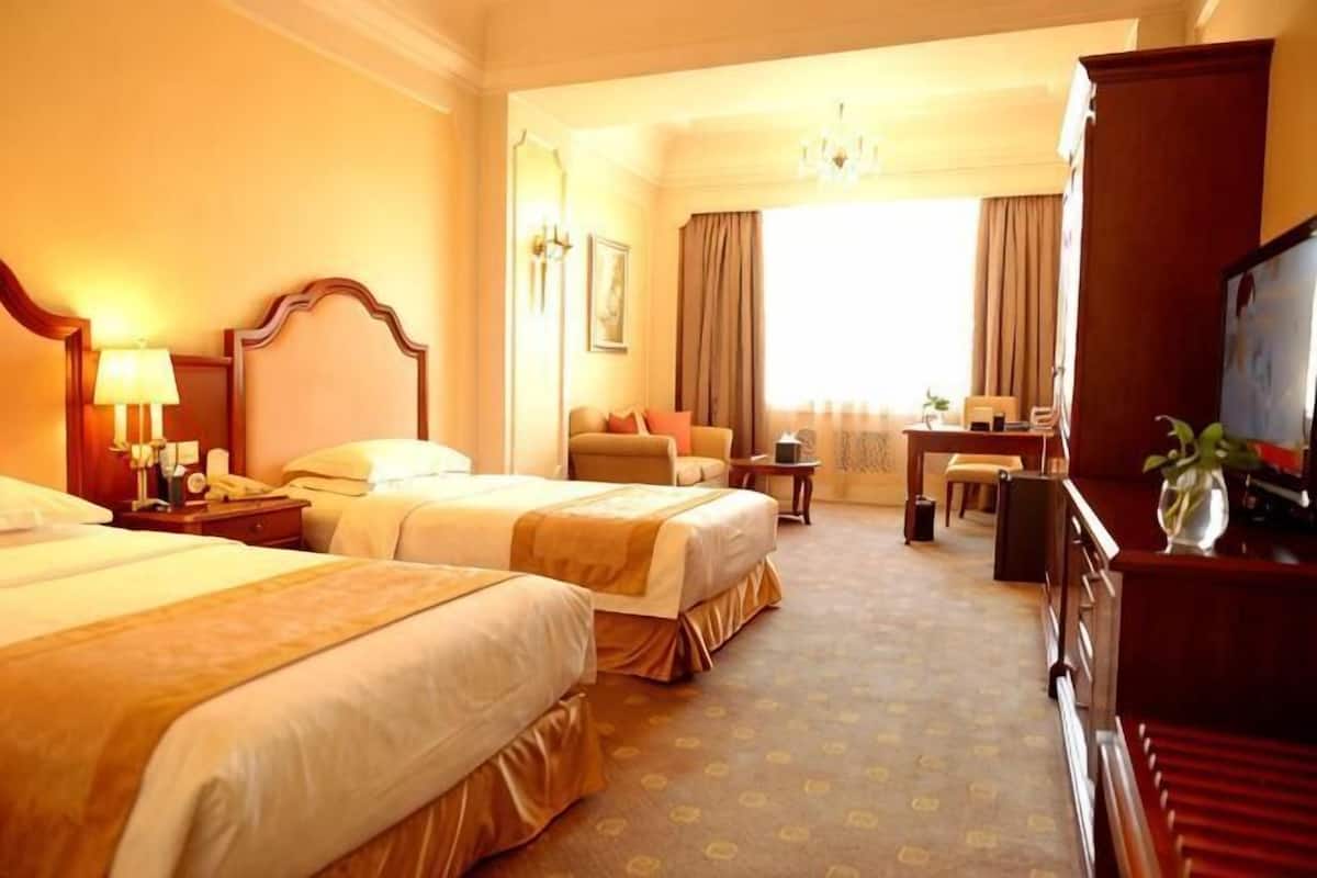 Ein Hotelzimmer mit zwei Betten, einem Schreibtisch, einem Sessel, einem Fernseher und einem großen Fenster.