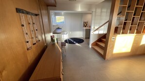 A spacious living area with a wooden bench, a small table with a plant, a staircase with a wooden railing, and a view of a kitchen area.