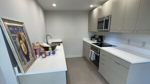 A modern kitchen with white cabinetry, a microwave, and a stove. There is a framed picture on the counter and some food items.