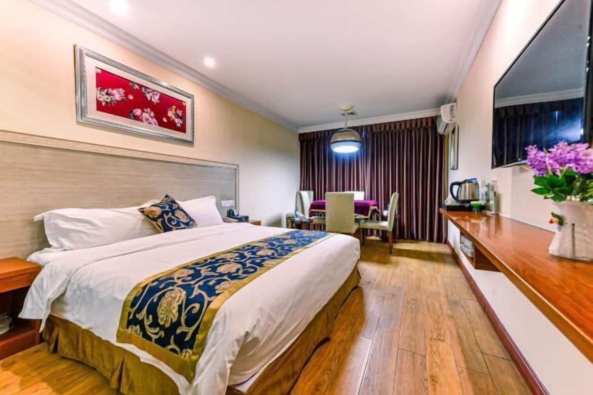 Habitación de hotel con una cama grande, un escritorio, una silla, una lámpara de escritorio, un espejo y un florero con flores.