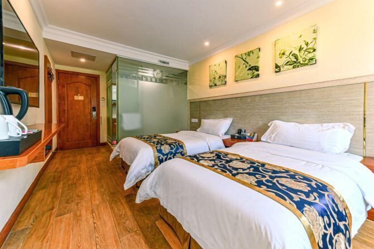 A hotel room with two beds, a wooden floor, a desk with a chair, and artwork on the wall.