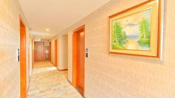A hotel hallway with doors, a carpeted floor, and a framed painting on the wall.