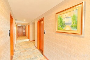 Een hotelgang met deuren, een vloerbedekking en een schilderij in een lijst aan de muur.