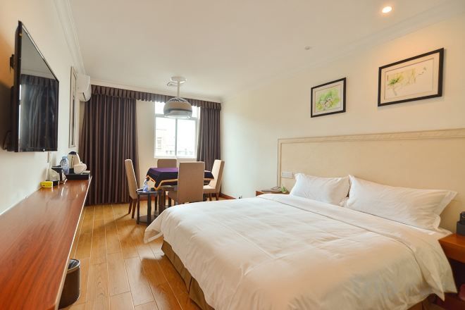 A hotel room with a bed, a desk, a chair, a TV, and a window with curtains.