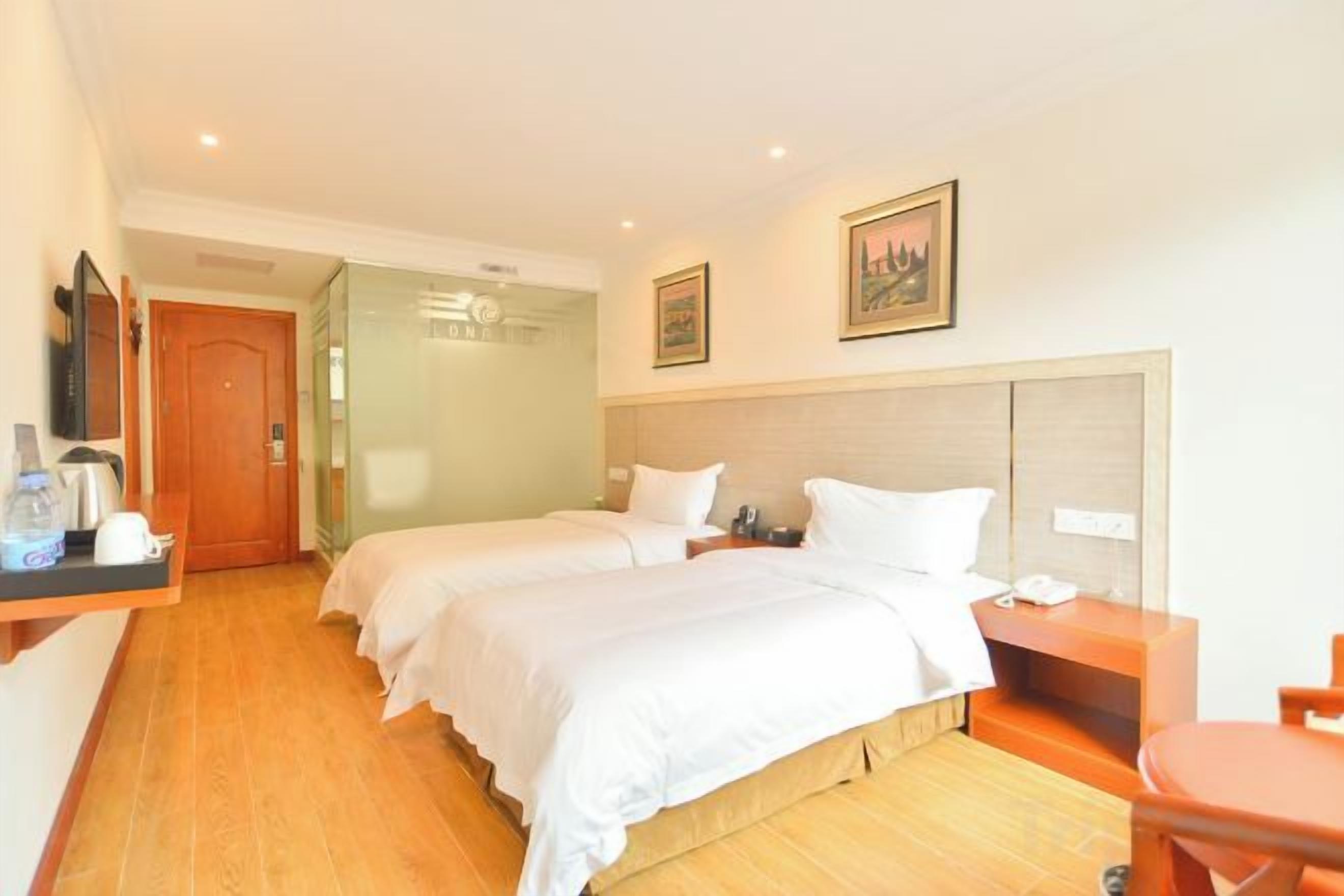 A hotel room with two beds, a desk, a chair, a TV, and a bathroom door.